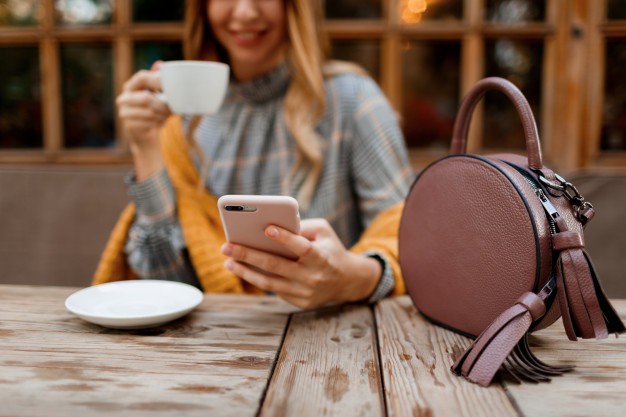 woman using mobile phone texting message drinking coffee stylish bag table wearing grey dress orange plaid enjoying cozy morning cafe 273443 2554